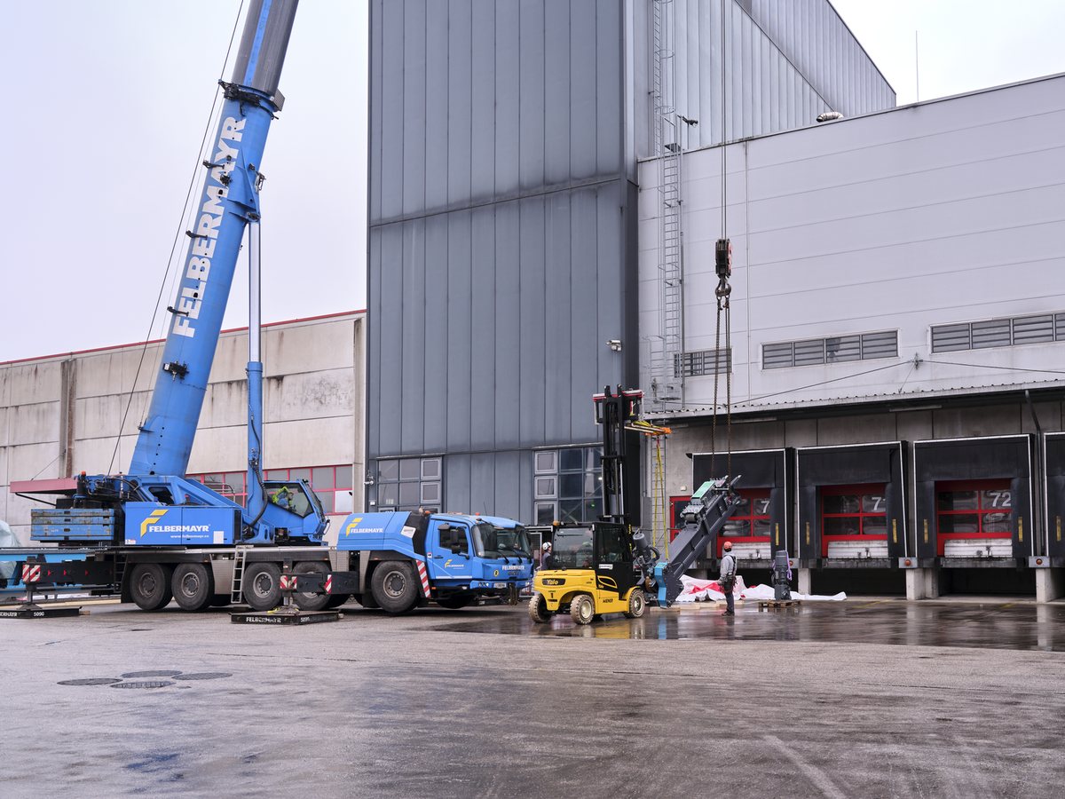 Grúa móvil y carretilla elevadora delante de las puertas de carga de la nave, listas para la izada