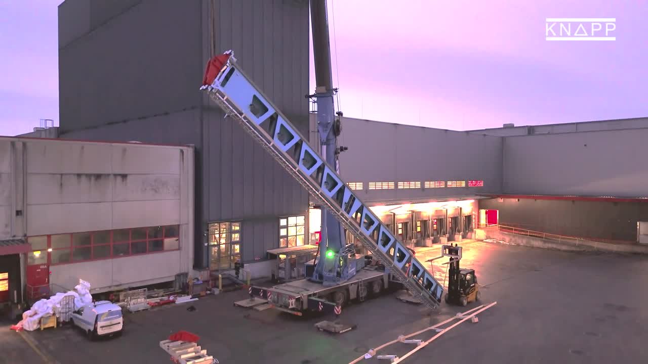 Imagen del vídeo: grúa elevando el mástil delante del centro de distribución de Spar